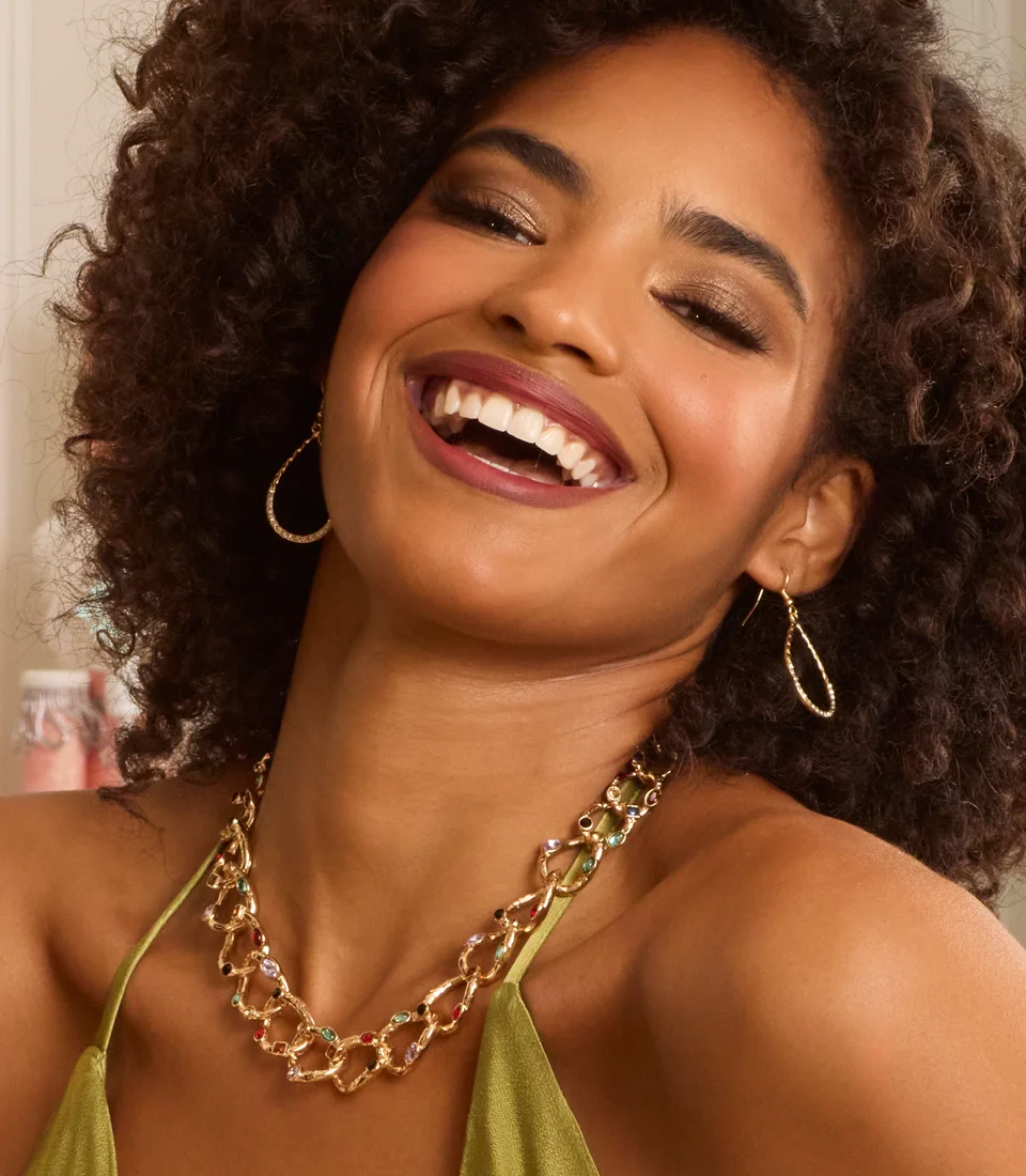 Model laughing in joy wearing gold gemmed jewelry, in a green dress