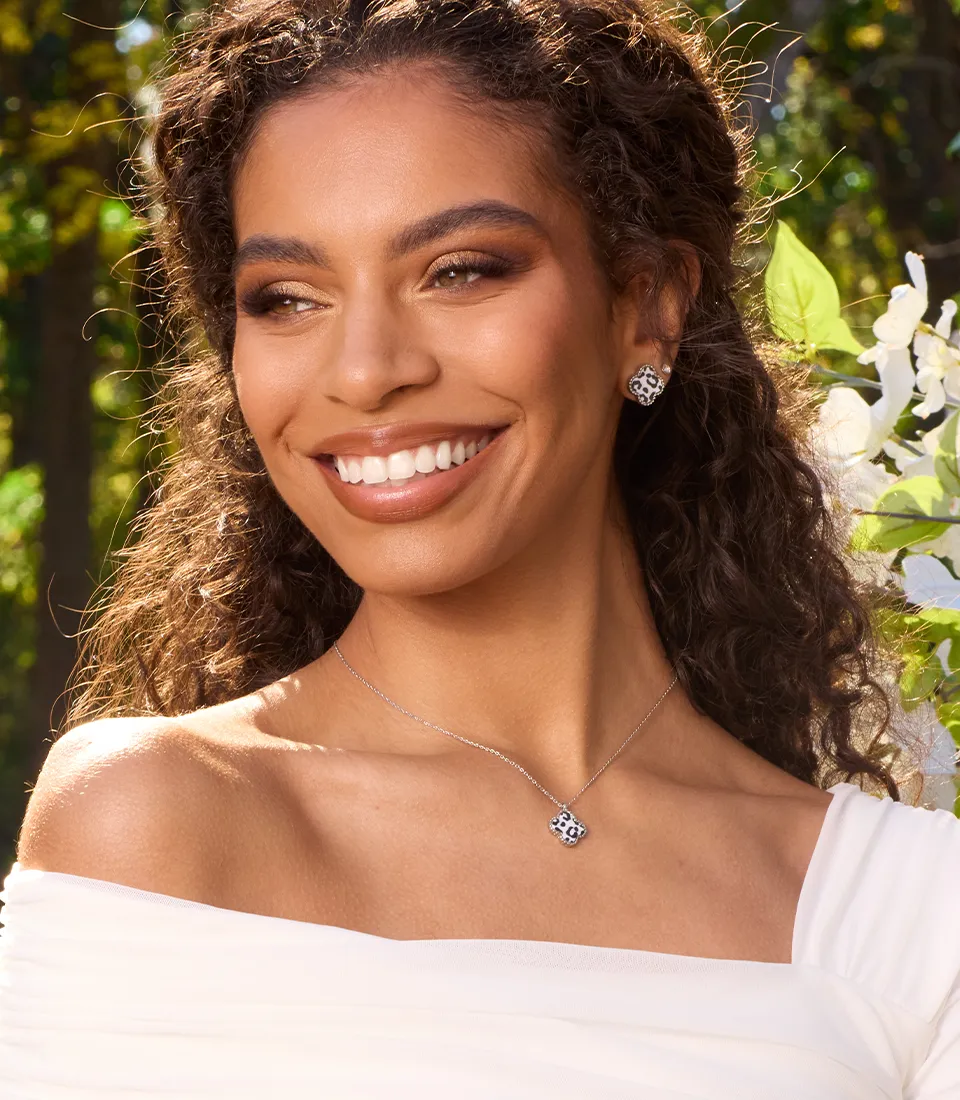 Model smiling proudly wearing a silver necklace with small cutout pendants on it