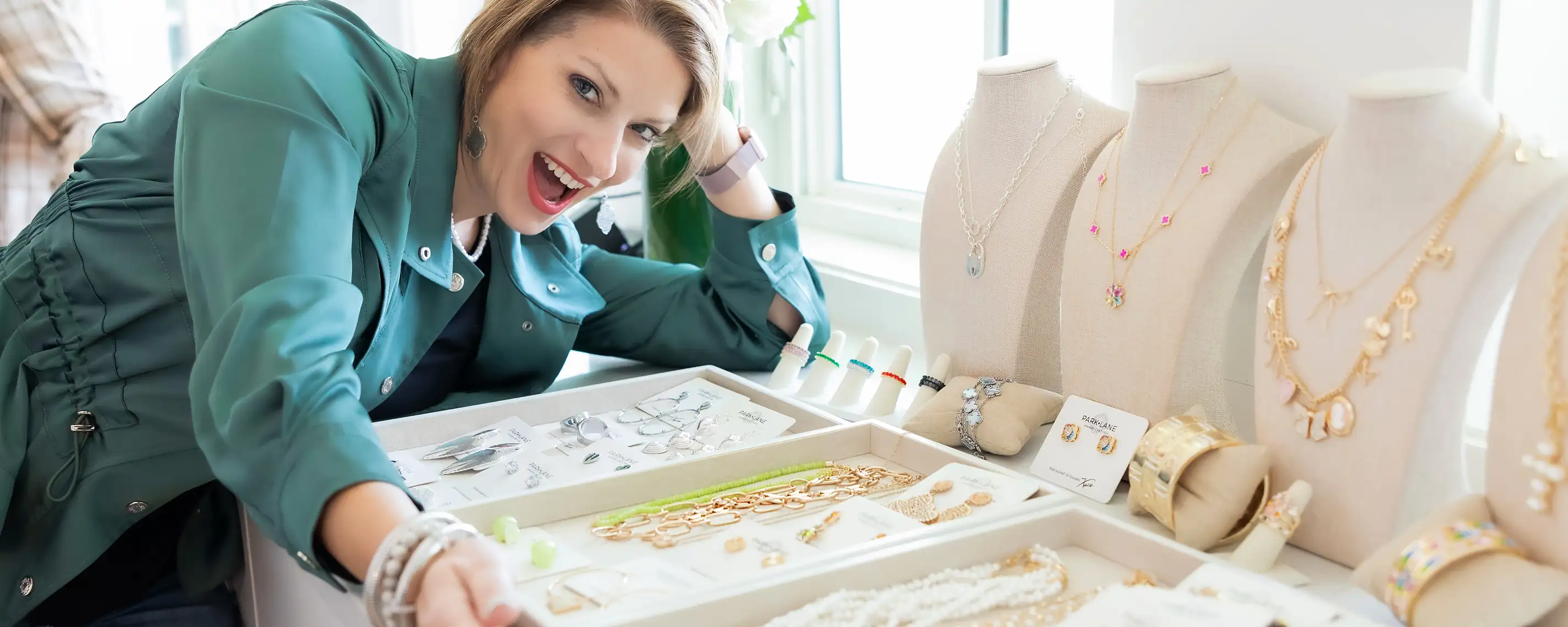 Model in green leaning over trays of jewelry, excitedly