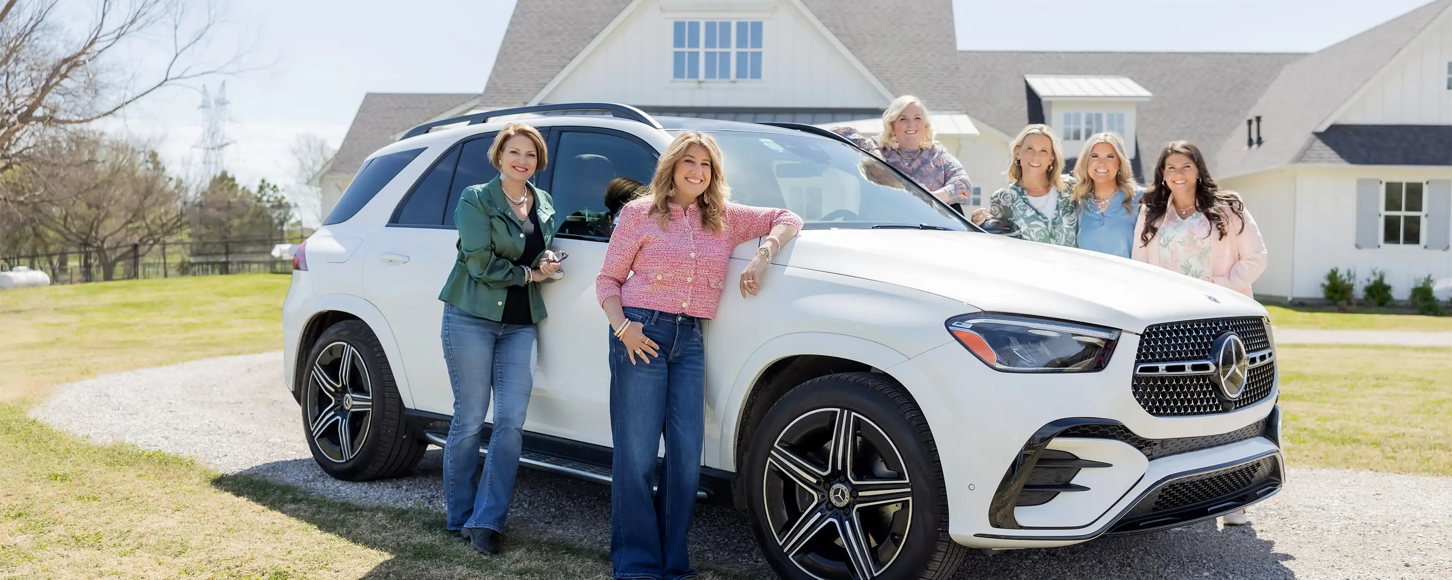 group of women standing around a brand new Mercedes SUV on a beautiful property